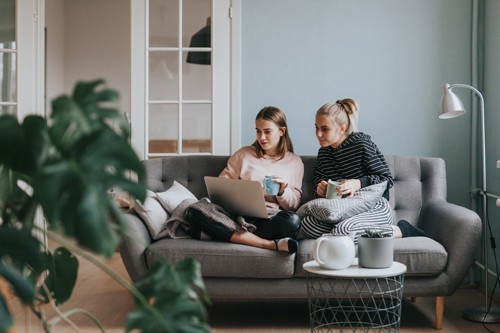 Two women sitting on a sofa together buying something on a laptop