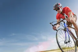 Man in red clothing riding a bike in the sunshine with blue clouds surrounding him