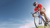 Man in red clothing riding a bike in the sunshine with blue clouds surrounding him