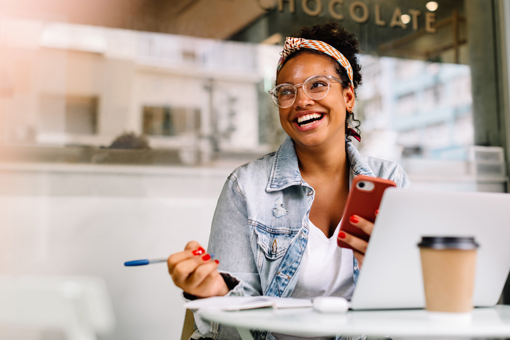 Woman Looking Into Distance Smiling Whilst Working On Laptop And Holding Pen