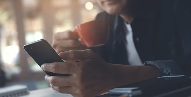 Man with a coffee looking at his phone with his laptop open