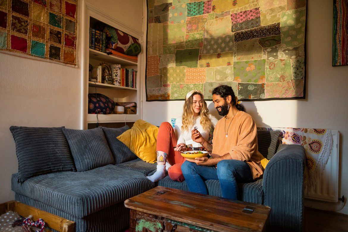 Man and woman sat on a blue sofa eating food