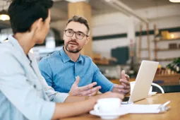 Two businesspeople talking over a coffee, looking at a laptop