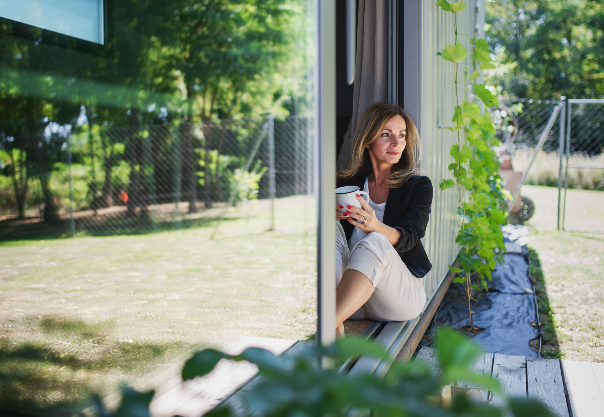 Woman sitting in the doorway of her summerhouse in the sunshine, admiring her plants