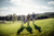 Three men walking across a golf course in the sunshine carrying their equipment