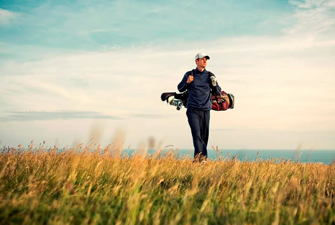Man walking across a golf course carrying golf clubs